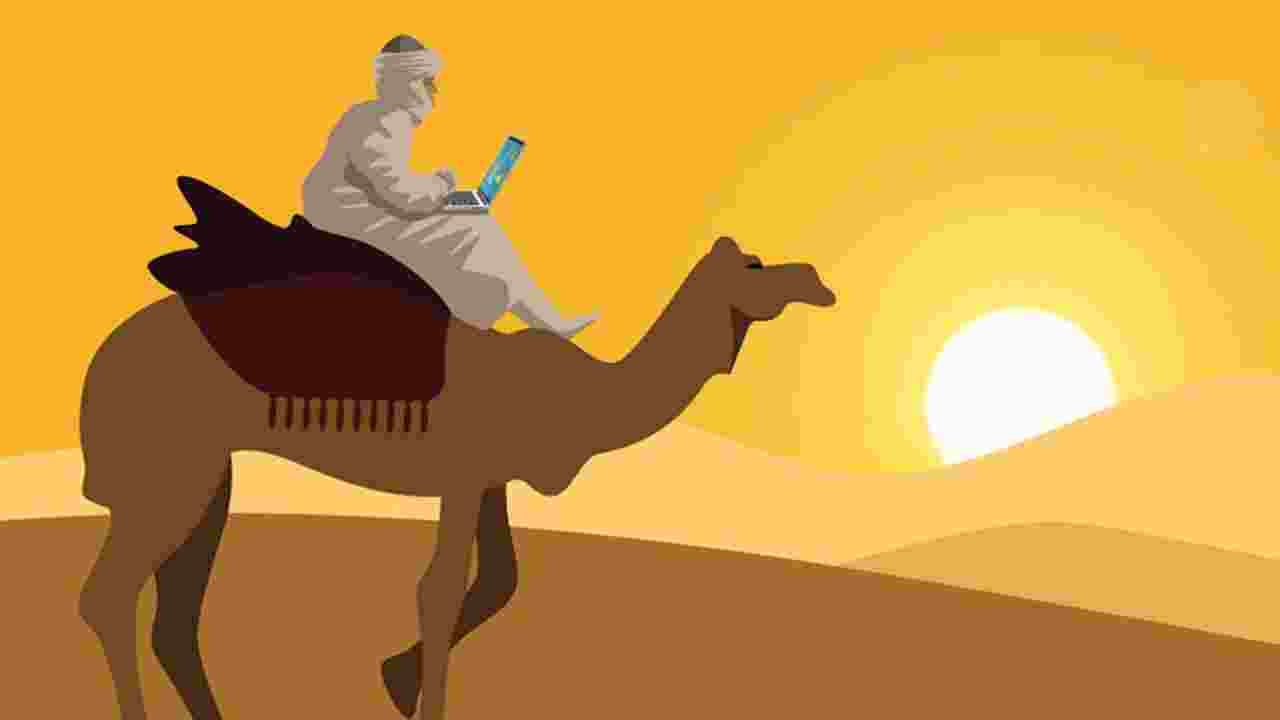 A digital nomad rides a camel across the desert while working remotely. 15.5 million American workers describe themselves as digital nomads.